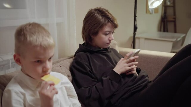 Young mother and her son wearing hearing aids share popcorn while laughing at a TV show. Warm living room scene showcasing joyful family bonding and inclusive representation. Focus on normalizing assi