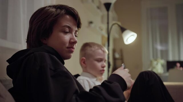 Young mother and her son wearing hearing aids share popcorn while laughing at a TV show. Warm living room scene showcasing joyful family bonding and inclusive representation. Focus on normalizing assi