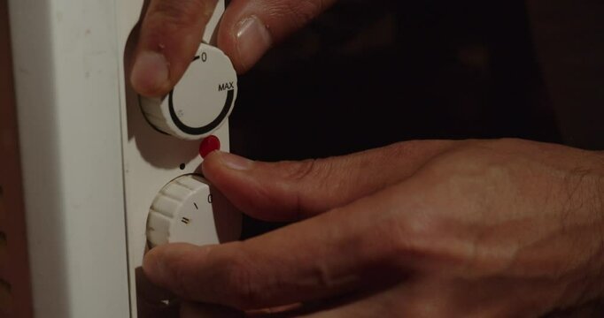 A hand turns on a convector with toggle switches and a light indicator. Heating. Consumption. Life activity