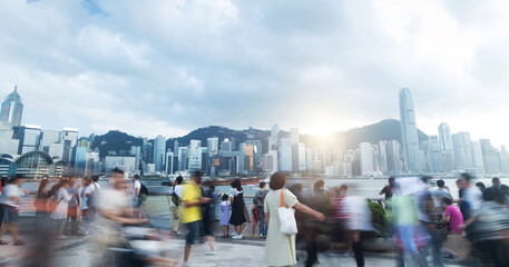 Tourists and citizens enjoying a cloudy day walking on the Hong Kong waterfront, with skyscrapers...