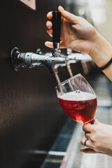Close-up of a hand pouring red beverage from a tap into a wine glass, captured during drink service...