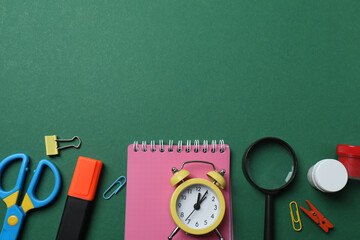 Top view of school supplies, pencils, erasers, paper clips and notebooks, on a green background....