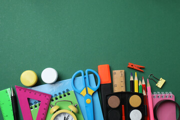 Top view of school supplies, pencils, erasers, paper clips and notebooks, on a green background....