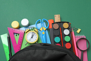 Top view of school supplies, pencils, erasers, paper clips and notebooks, on a green background....