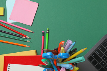 Top view of school supplies, pencils, erasers, paper clips and notebooks, on a green background....