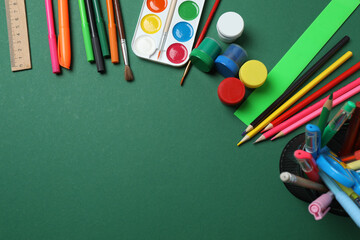 Top view of school supplies, pencils, erasers, paper clips and notebooks, on a green background....