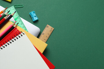 Top view of school supplies, pencils, erasers, paper clips and notebooks, on a green background....