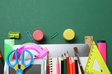 Top view of school supplies, pencils, erasers, paper clips and notebooks, on a green background....