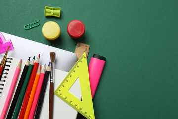 Top view of school supplies, pencils, erasers, paper clips and notebooks, on a green background....
