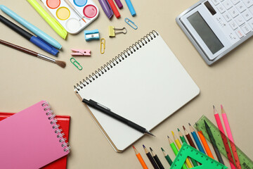 Top view of school supplies, pencils, erasers, paper clips and notebooks, on a beige background....