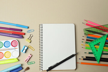 Top view of school supplies, pencils, erasers, paper clips and notebooks, on a beige background....