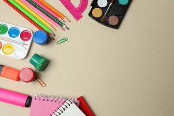 Top view of school supplies, pencils, erasers, paper clips and notebooks, on a beige background....