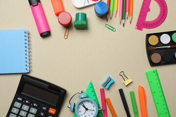 Top view of school supplies, pencils, erasers, paper clips and notebooks, on a beige background....