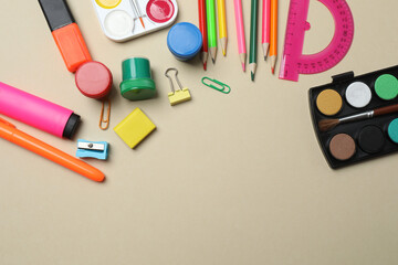 Top view of school supplies, pencils, erasers, paper clips and notebooks, on a beige background....