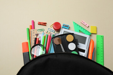 Top view of school supplies, pencils, erasers, paper clips and notebooks, on a beige background....