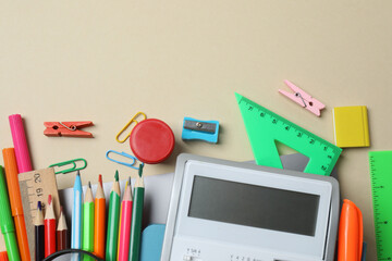Top view of school supplies, pencils, erasers, paper clips and notebooks, on a beige background....