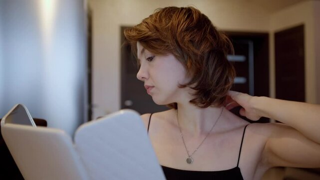 A woman gets ready for a date, applying makeup and styling her hair in front of a living room mirror. Authentic preparation routine capturing natural beauty rituals