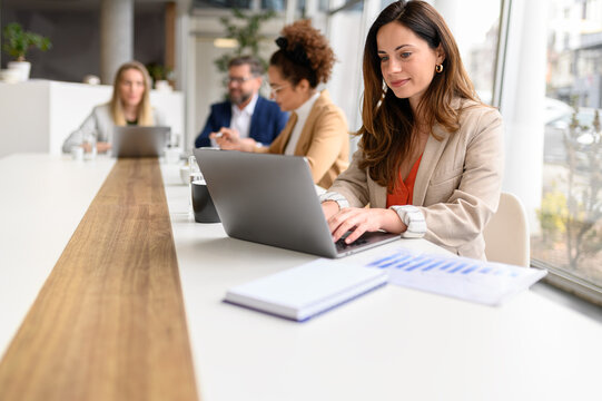 Focused businesswoman typing on laptop and analyzing data with colleagues in modern office during team meeting - Powered by Adobe