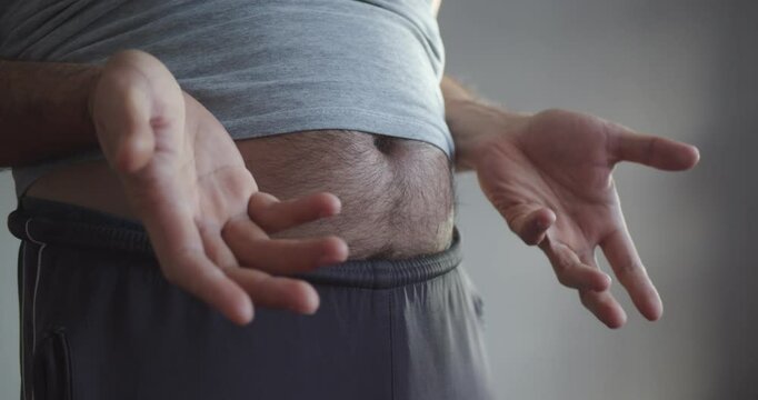 Modern Adult man in sweatpants and a T-shirt with a bare hairy beer belly actively gesticulates. Close-up on the stomach and arms