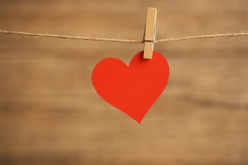 A red heart dangling on a clothesline with a blurry backdrop
