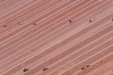 Textured surface of an aged corrugated iron roof covered in rich reddish brown rust with visible fasteners creating a rustic pattern