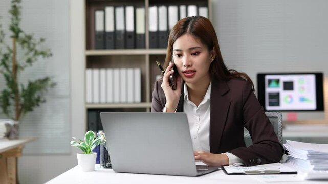 Businesswoman engaging in serious phone conversation at work desk. Professional businesswoman multitasking during intense workplace communication.