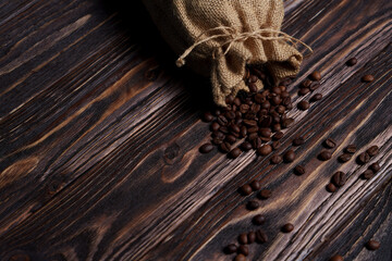 Coffee beans spilling from burlap sack onto dark wooden surface