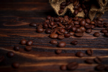 Coffee beans spilling from burlap sack onto dark wooden surface