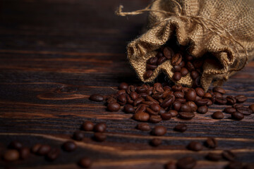 Coffee beans spilling from burlap sack onto dark wooden surface