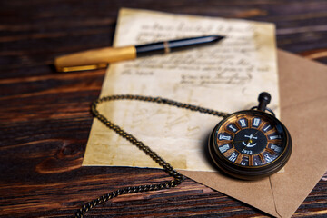 Vintage pocket watch with handwritten letter and pen on wooden surface