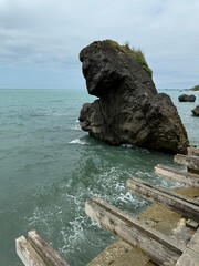 Large coastal rock near wooden beams over the sea with cloudy sky. Suitable for travel, geology,...