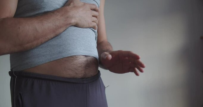An adult man in sweatpants and a T-shirt with a bare hairy beer belly actively gesticulates. Close-up on the stomach and arms