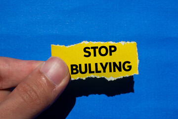 Stop bullying message written on ripped torn yellow paper piece on blue background. Conceptual stop...