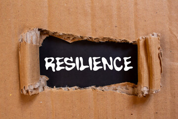 Resilience message written on ripped torn cardboard paper on black background. Conceptual...