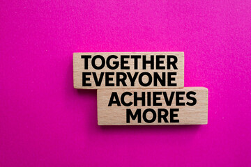 Together everyone achieves more message written on wooden blocks on pink background. Conceptual...