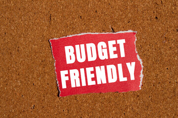 Budget friendly message written on ripped torn red paper piece on brown background. Conceptual...