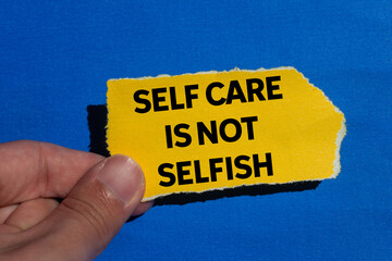 Self care is not selfish message written on ripped torn yellow paper piece on blue background....