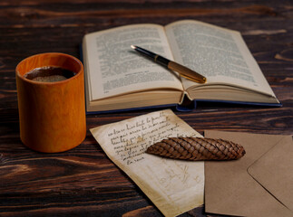 Coffee cup with open book, pen, pine cone, and letter on wooden table