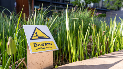 Caution sign beside garden pond warning of shallow water