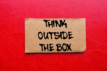 Think outside the box message written on ripped torn cardboard paper piece on red background....