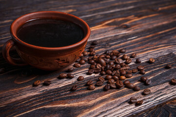 Cup of black coffee with scattered coffee beans on dark wooden table