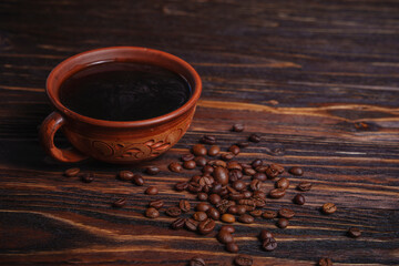 Cup of black coffee with scattered coffee beans on dark wooden table