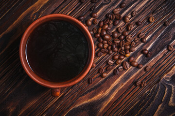 Cup of black coffee with scattered coffee beans on dark wooden table