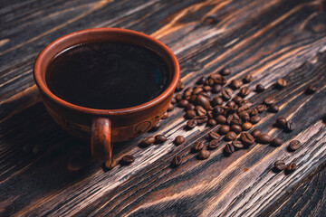 Cup of black coffee with scattered coffee beans on dark wooden table