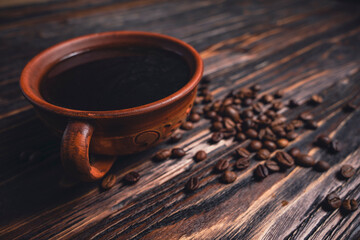Cup of black coffee with scattered coffee beans on dark wooden table