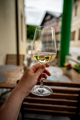 Hand holding a glass of white wine at outdoor terrace with blurred urban background