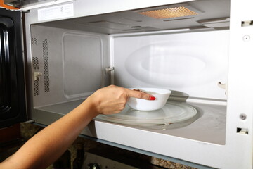 Women hand put food in white bowl in microwave oven