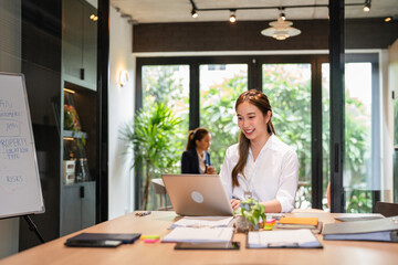 Obraz premium Asian business woman using laptop computer typing And working online sitting at desk in office . Office worker lady browsing internet on computer.