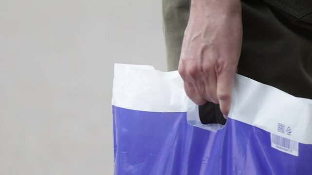 Person is holding a blue plastic bag. The bag has a white handle. The bag is in the person's hand