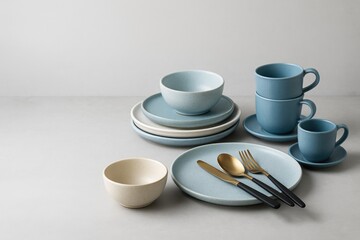 Elegant ceramic tableware set with cups and utensils on a soft grey surface, blank space for customization